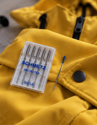 Packung Microtex-Nähmaschinennadeln Stärke 90/14 und einzelne Nadel auf gelber Softshelljacke